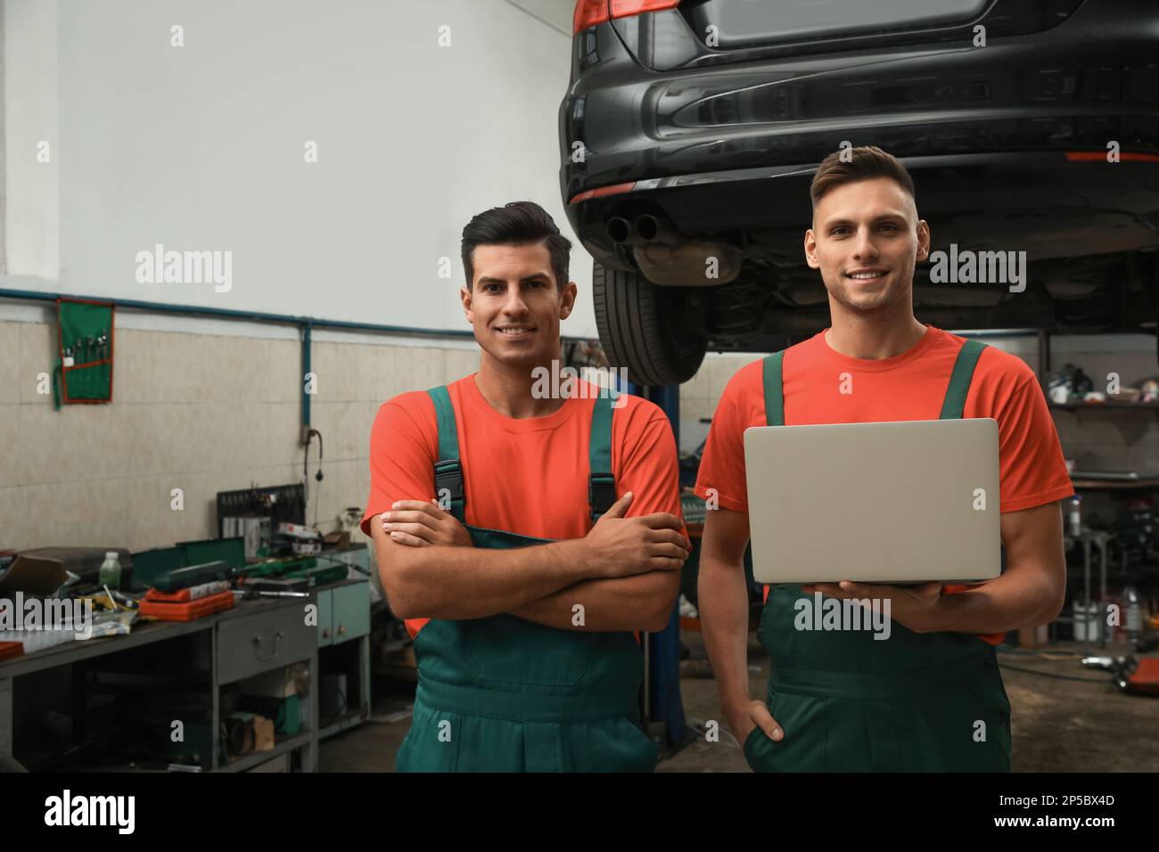 Mechanics with laptop near lifted car at automobile repair shop Stock