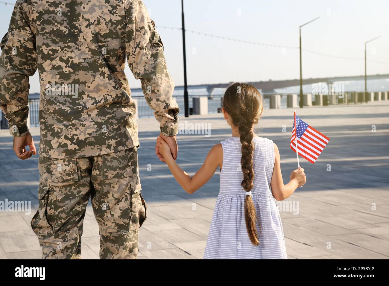 Soldier and his little daughter with American flag outdoors, back view. Veterans Day in USA Stock Photo