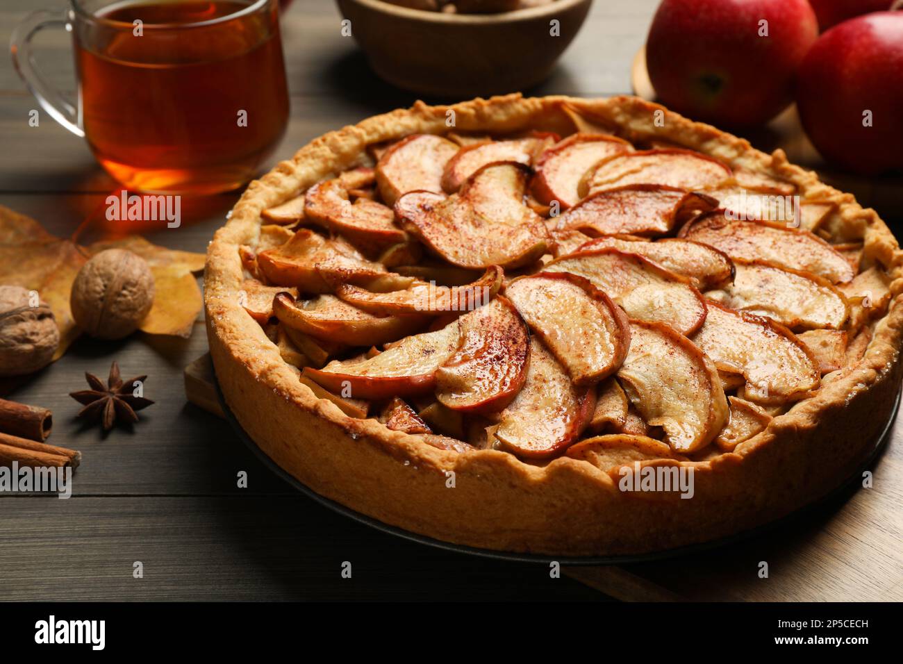Delicious apple pie, ingredients and cup of tea on wooden table, closeup Stock Photo