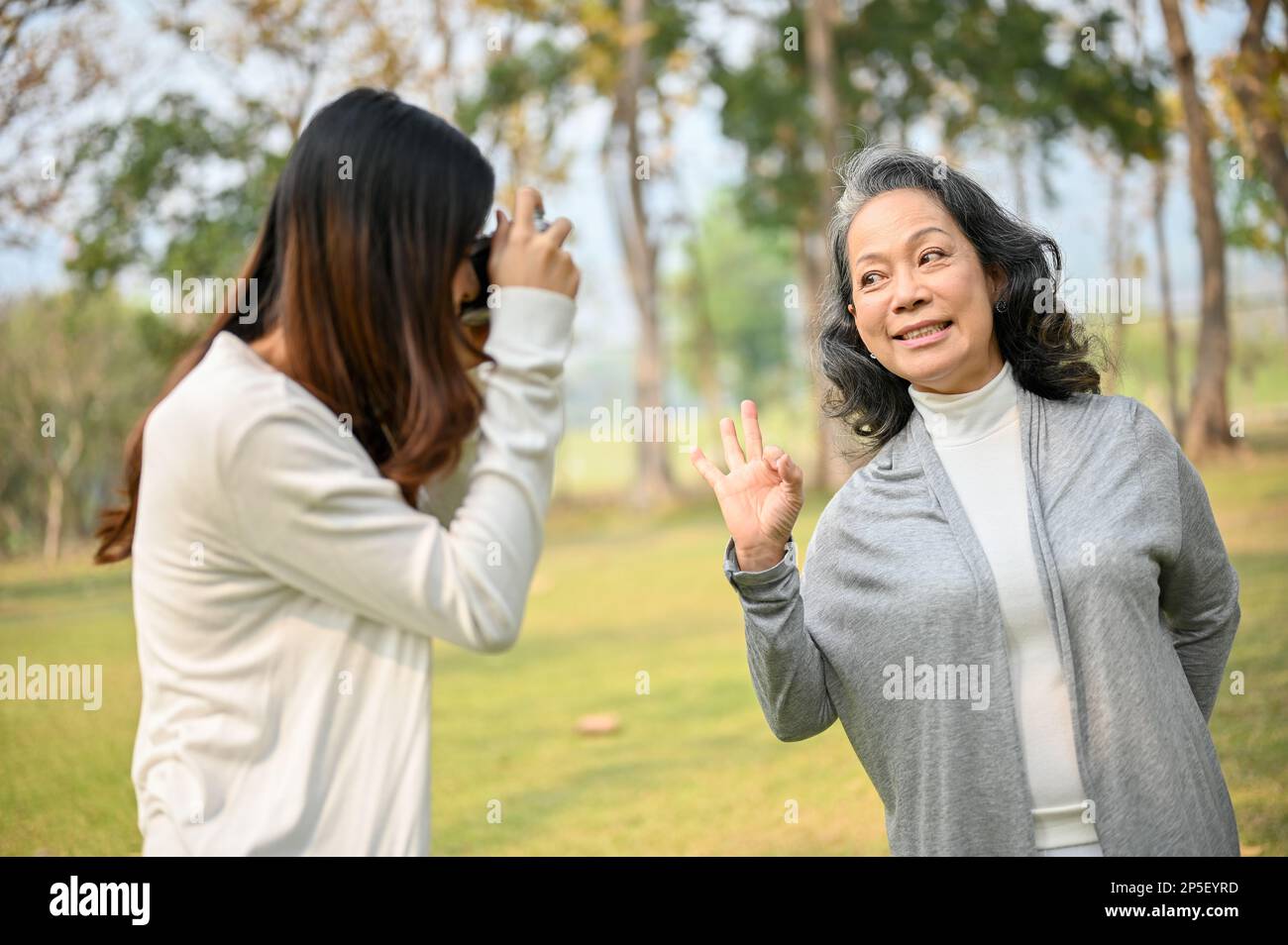 Lovely Asian granddaughter taking a picture of her happy grandmother with retro camera while spending time together in the beautiful green park. leisu Stock Photo