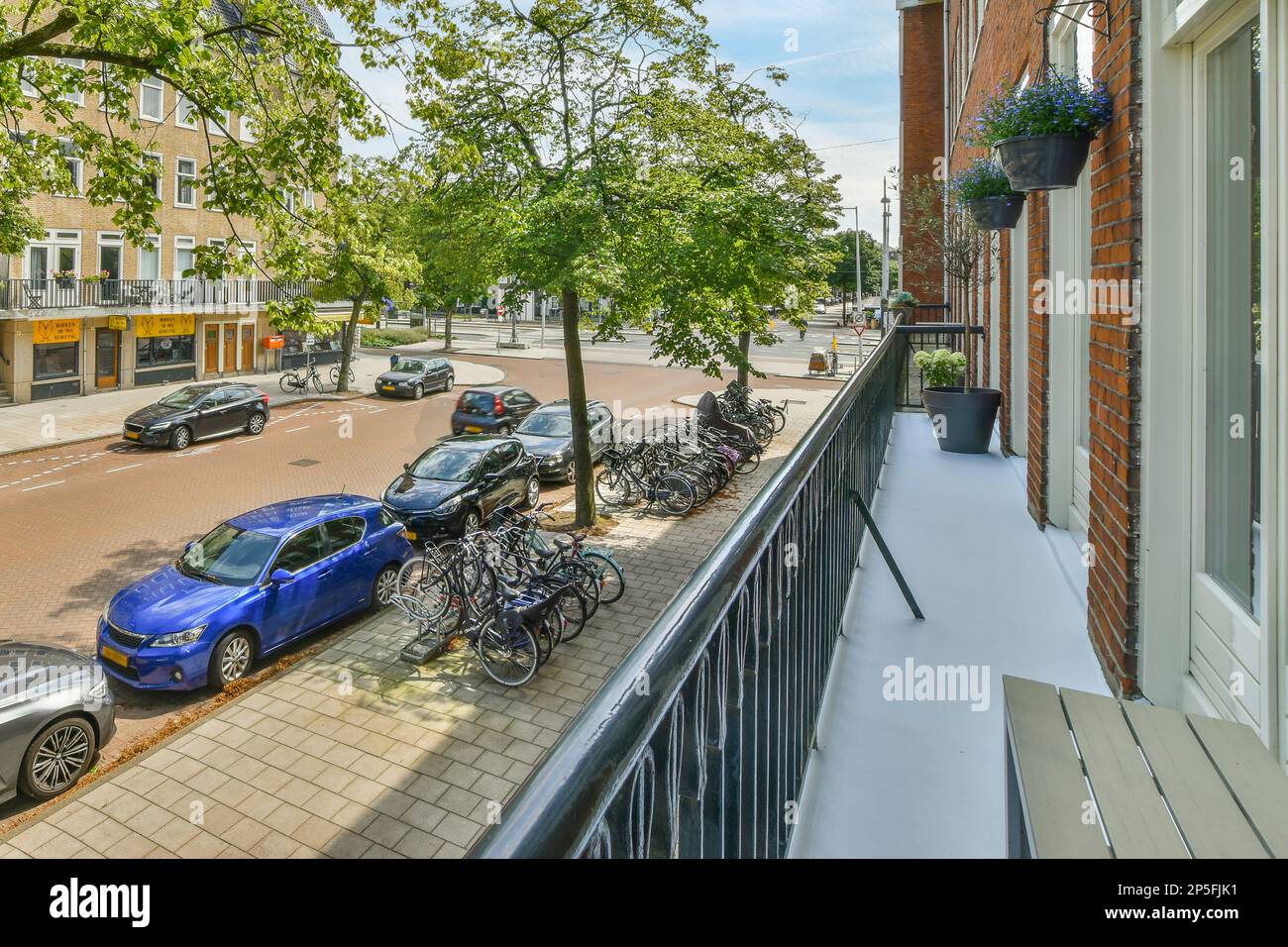 some bikes parked on the side of a street next to an apartment building with a tree in the front yard Stock Photo