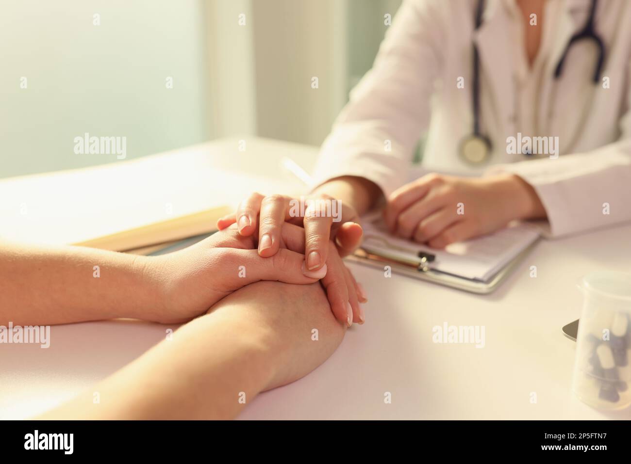 Doctor puts her hand on hands of patient, sitting with her in medical clinic. Stock Photo