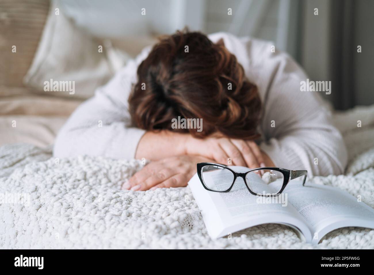 Sleeping middle aged woman withbook lying on bed at home Stock Photo