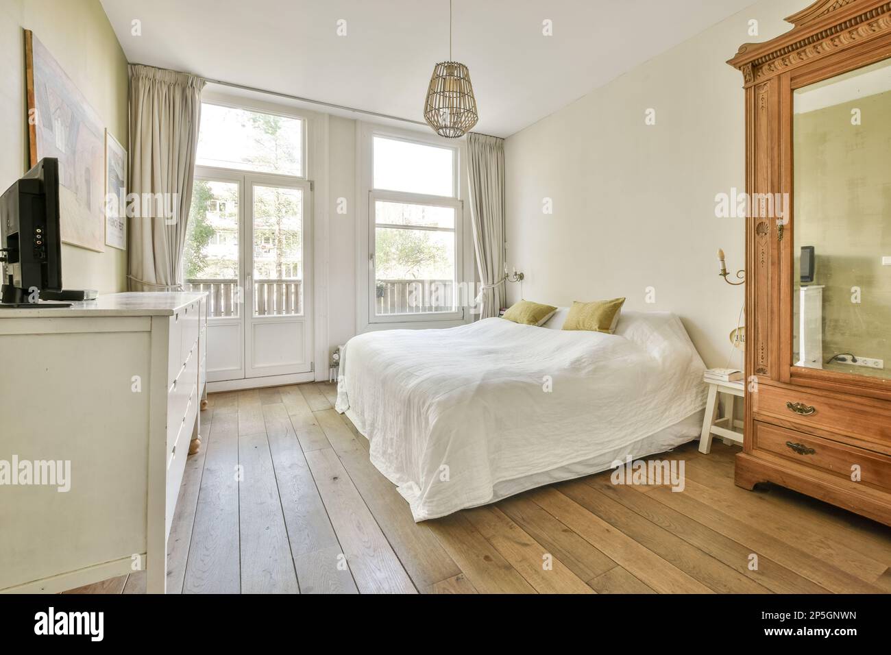 a bedroom with a bed, dresser and mirror in front of the window that looks  out to the garden outside Stock Photo - Alamy