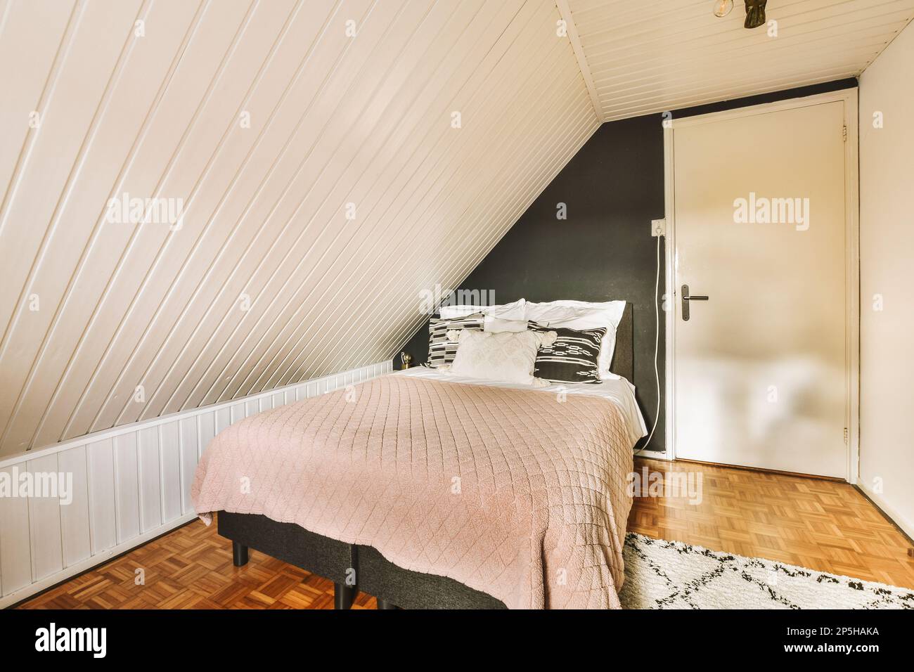 a bed in a room with white walls and wood flooring on the wall, there is a  pink comforter Stock Photo - Alamy