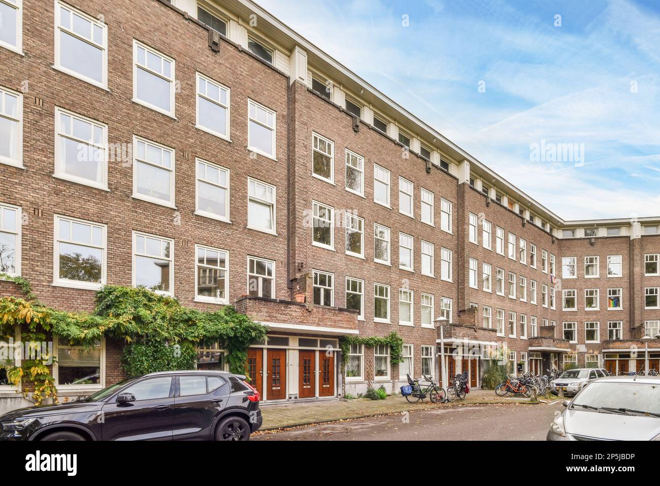 an apartment complex with cars parked on the street and people walking ...