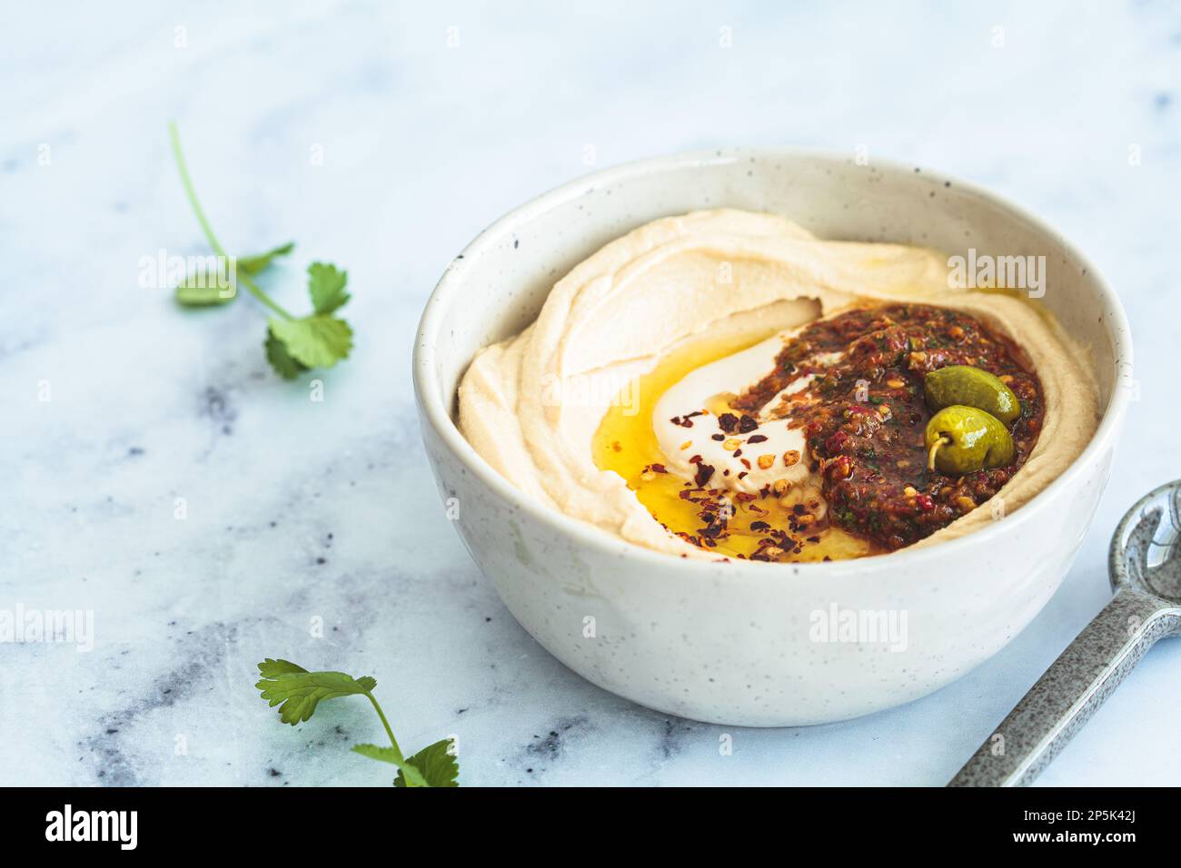 Homemade spicy hummus with tahini and olive oil in a bowl, white marble