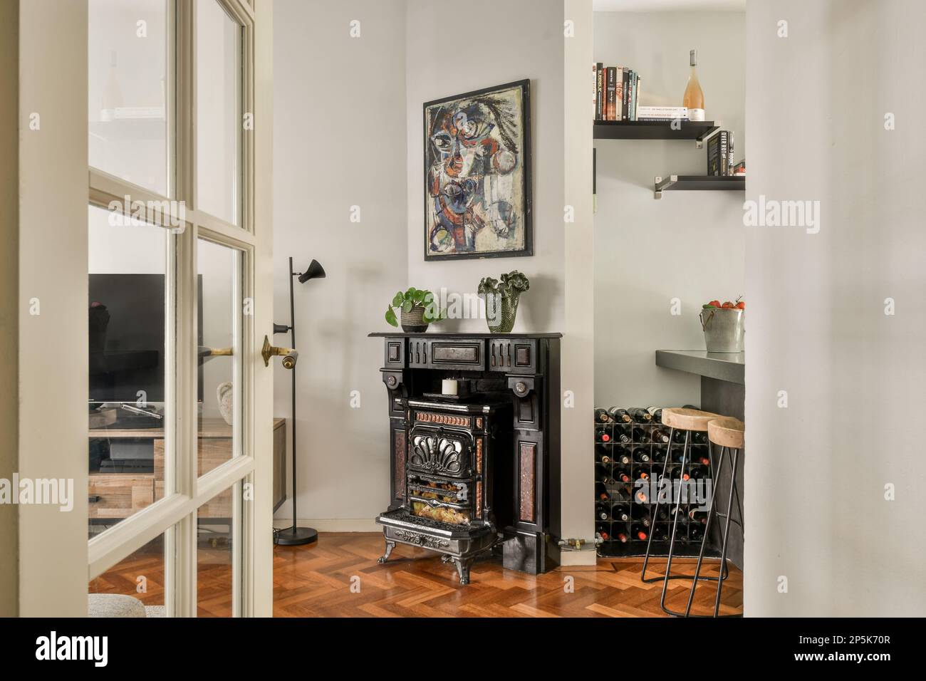 a living room with wood flooring and an open door leading to a wine cellar in the room is framed by white walls Stock Photo