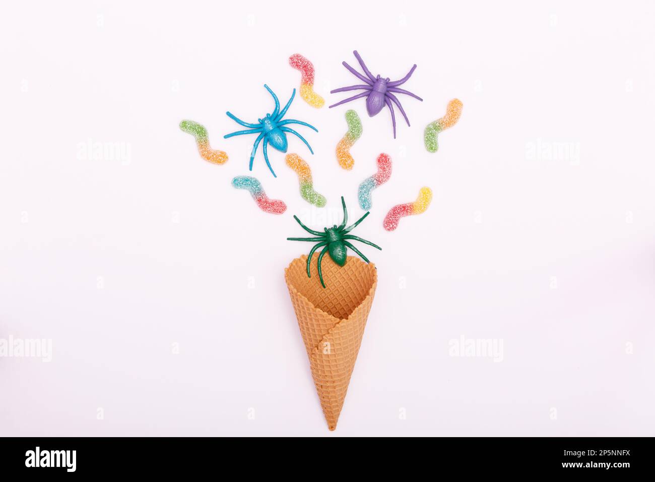 Halloween concept. Multicolored spiders, jelly candy worms and an ice cream cone on a white background. Flat lay, copy space, minimalism. High quality Stock Photo