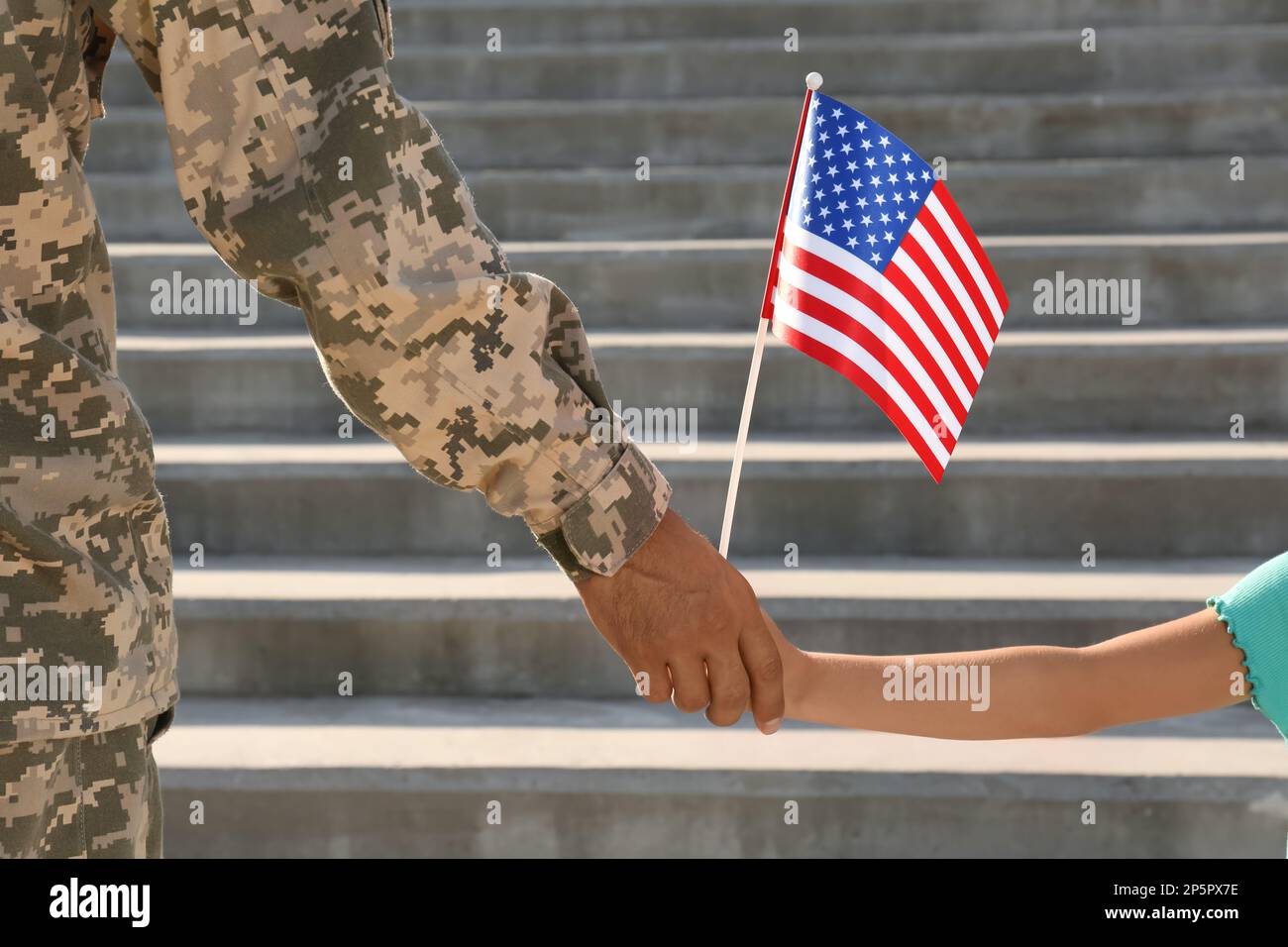 Soldier and his little daughter with American flag holding hands outdoors, closeup. Veterans Day in USA Stock Photo