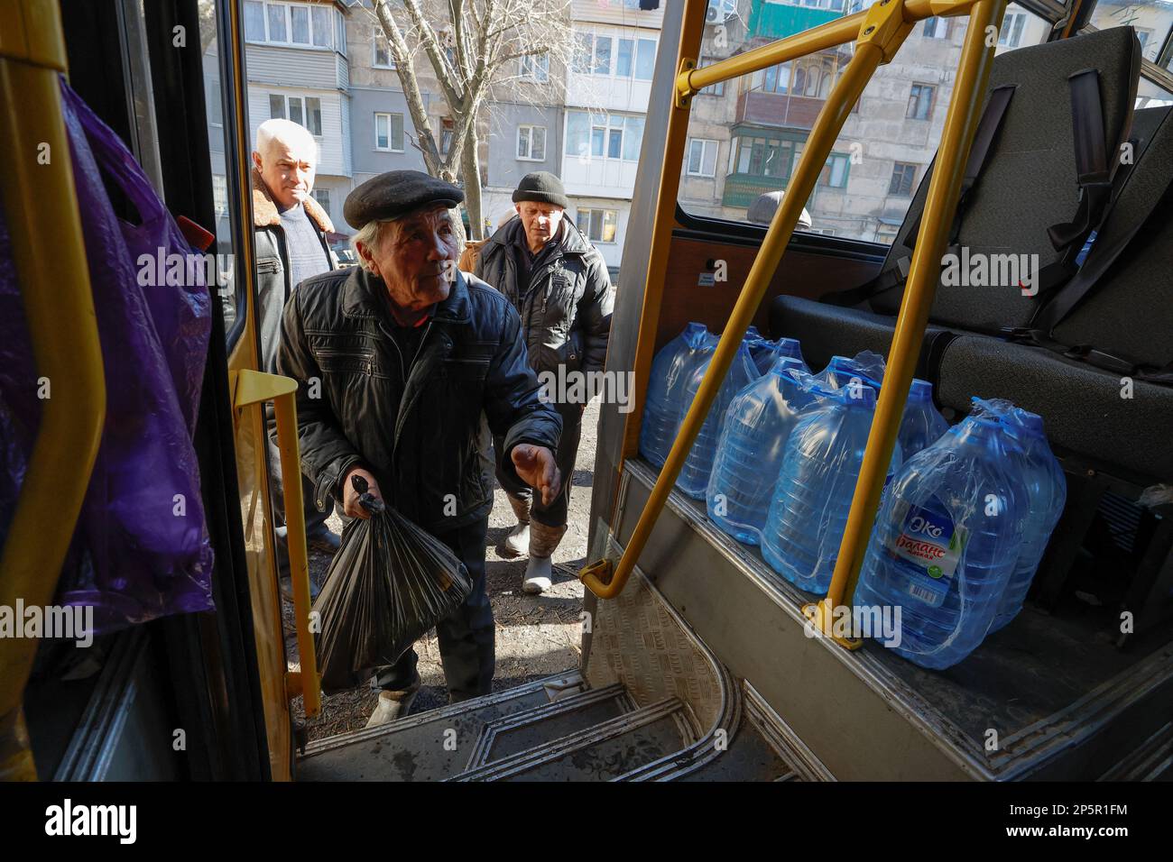 Men wait before receiving bottles with water and hand sanitizer and carrying them towards a library, as local residents come there to get warm, charge their electric devices, read books and daily newspapers in the course of Russia-Ukraine conflict in the town of Zolote (Zolotoye) in the Luhansk region, Russian-controlled Ukraine, March 6, 2023. REUTERS/Alexander Ermochenko Stock Photo