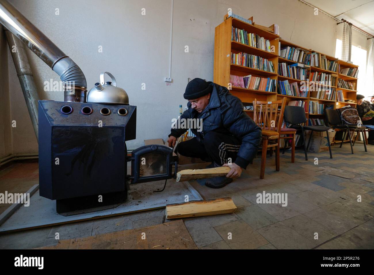 Local resident Igor, 56, who didn't give his family name, sits on his haunches in front of a furnace, as people come to a library to get warm, charge their electric devices, read books and daily newspapers in the course of Russia-Ukraine conflict in the town of Zolote (Zolotoye) in the Luhansk region, Russian-controlled Ukraine, March 6, 2023. REUTERS/Alexander Ermochenko Stock Photo