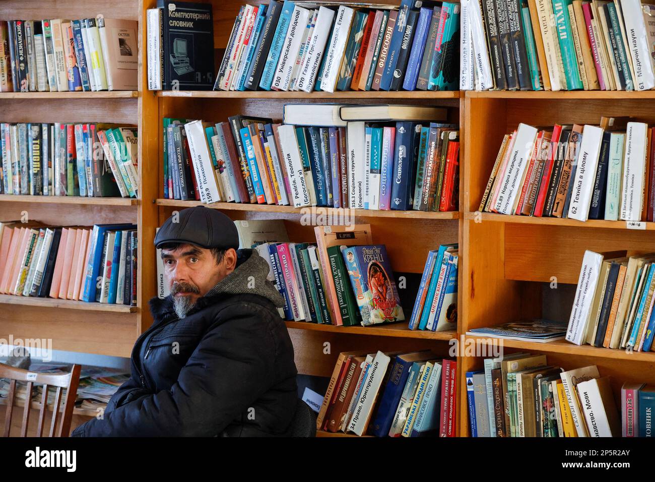 A man sits next to bookshelves, as local residents come to a library to get warm, charge their electric devices, read books and daily newspapers in the course of Russia-Ukraine conflict in the town of Zolote (Zolotoye) in the Luhansk region, Russian-controlled Ukraine, March 6, 2023. REUTERS/Alexander Ermochenko Stock Photo