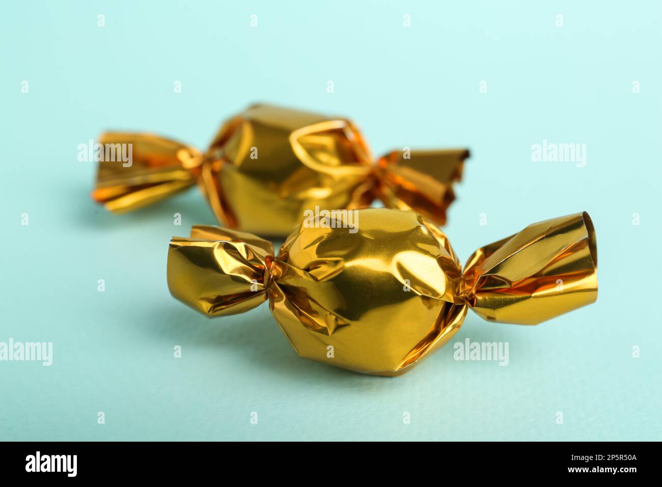 Candies in golden wrappers on light blue background, closeup Stock