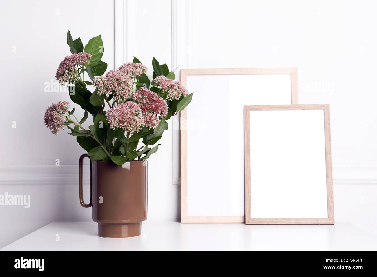 Stylish ceramic vase with beautiful flowers and blank frames on table ...