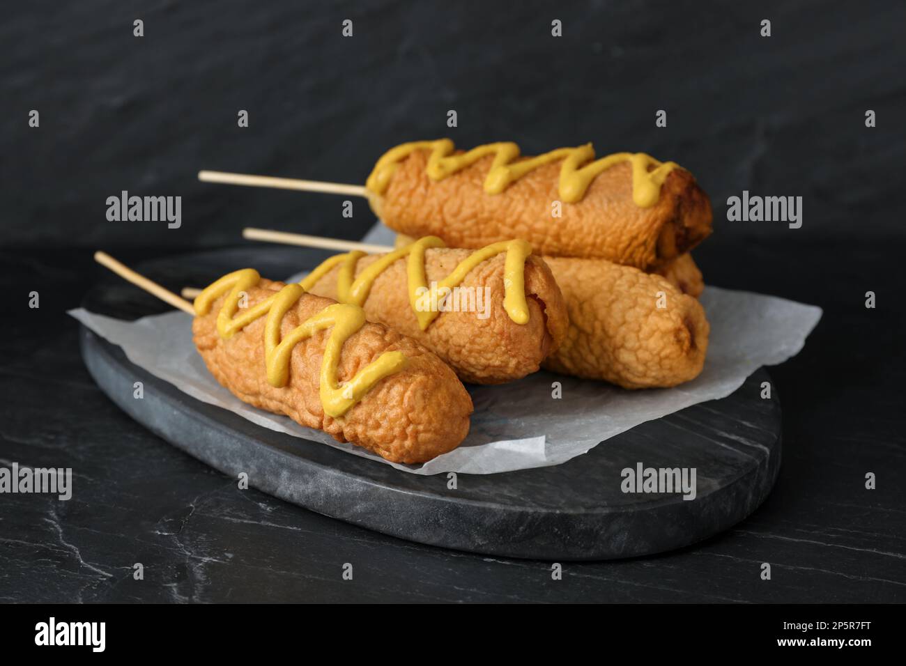 Delicious deep fried corn dogs with mustard on black table Stock Photo