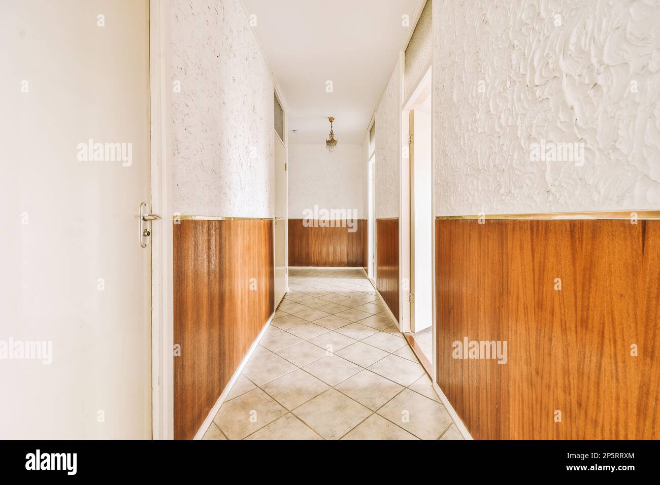 a long hallway with wood paneled walls and tile flooring on either side of the room, there is an open door leading Stock Photo