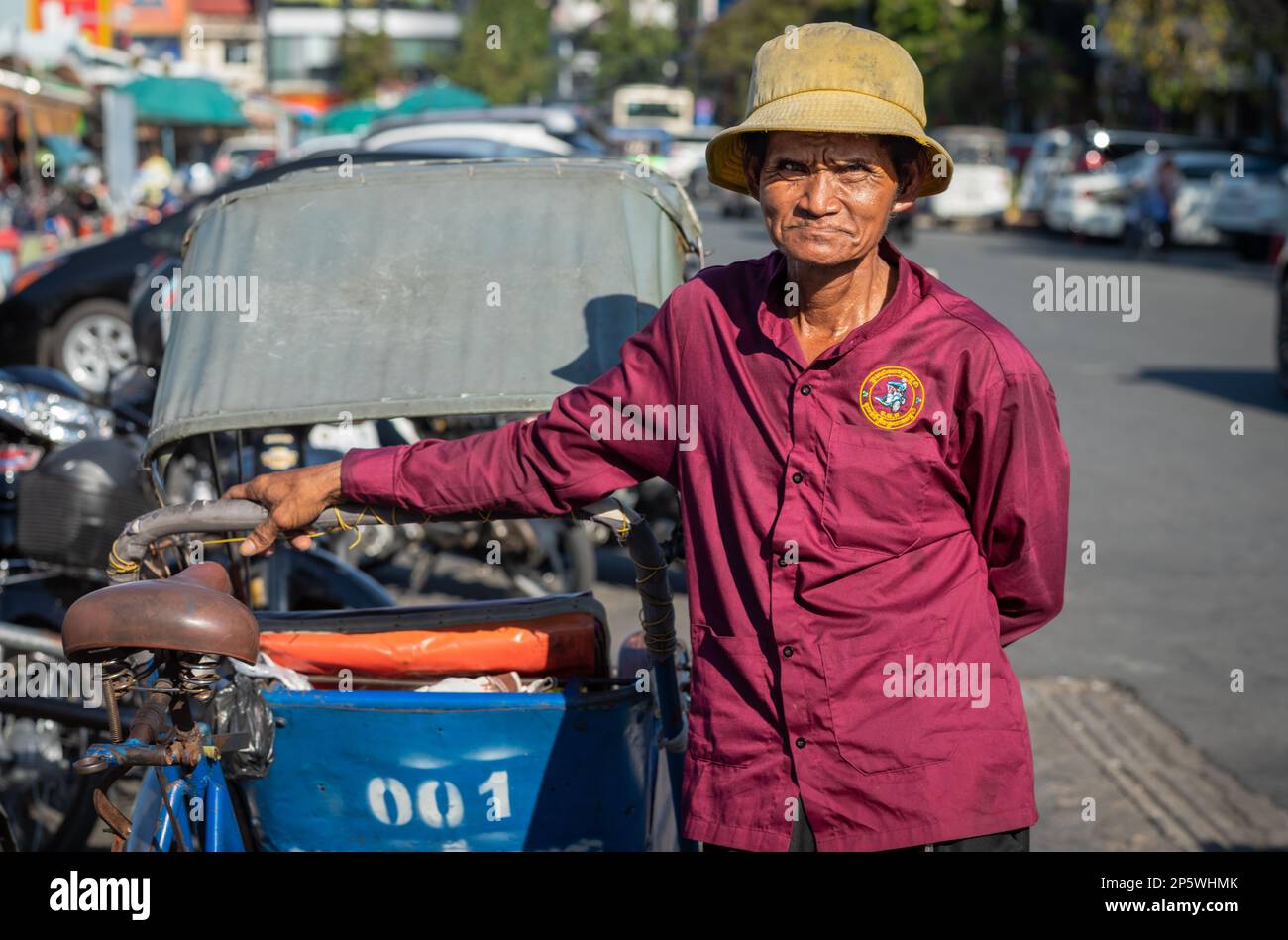 An elderly cyclo driver stands by his pedicab as he waits for passengers outside the Central Market in Phnom Penh, Cambodia. Stock Photo