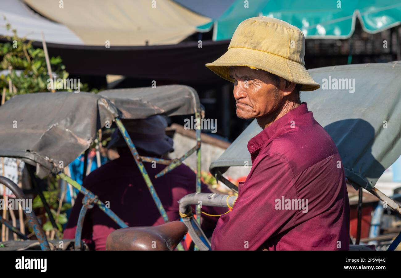 An elderly cyclo driver stands by his pedicab as he waits for passengers outside the Central Market in Phnom Penh, Cambodia. Stock Photo