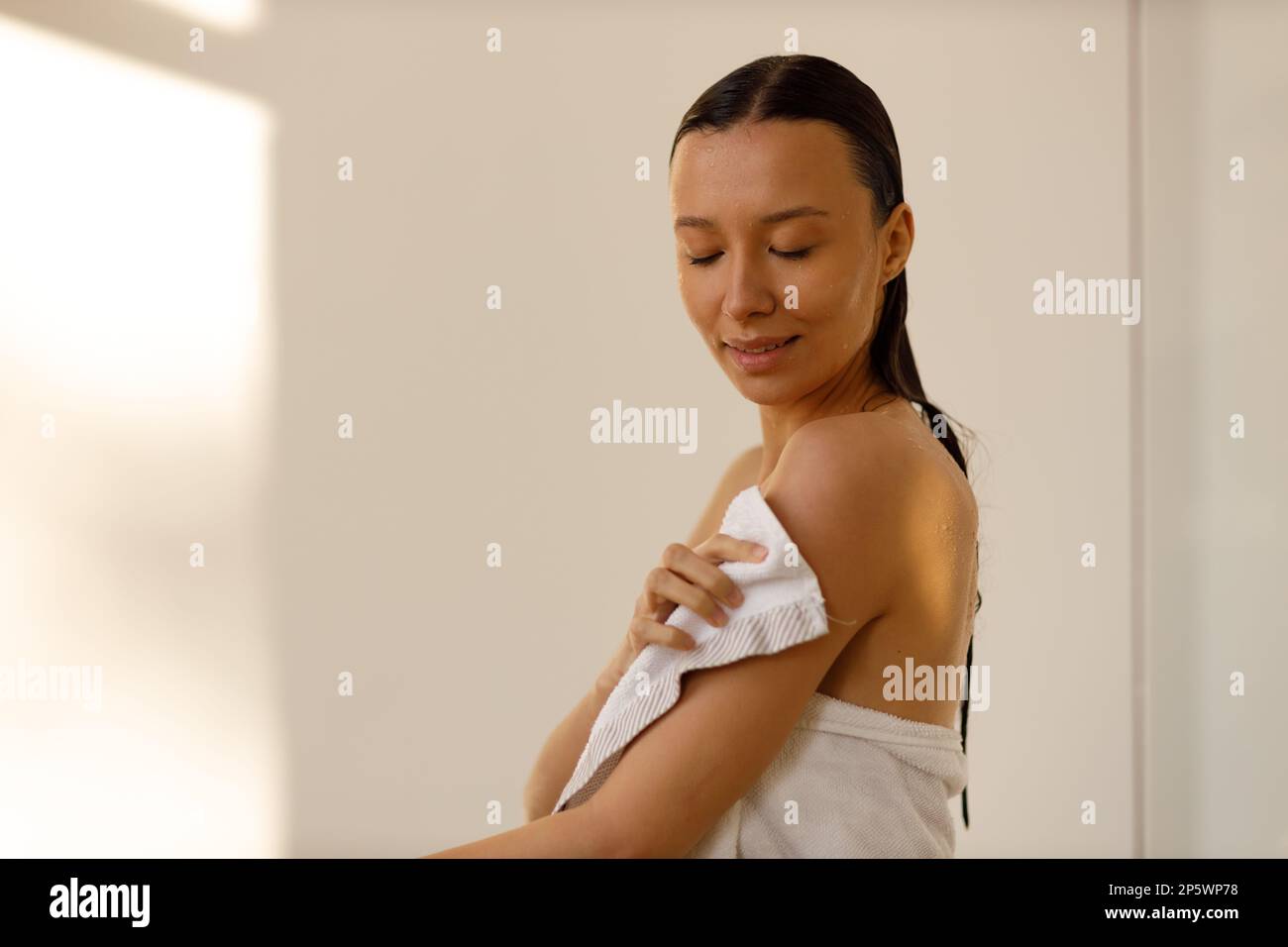 Beautiful young woman wrapping herself in white bath towel in shower
