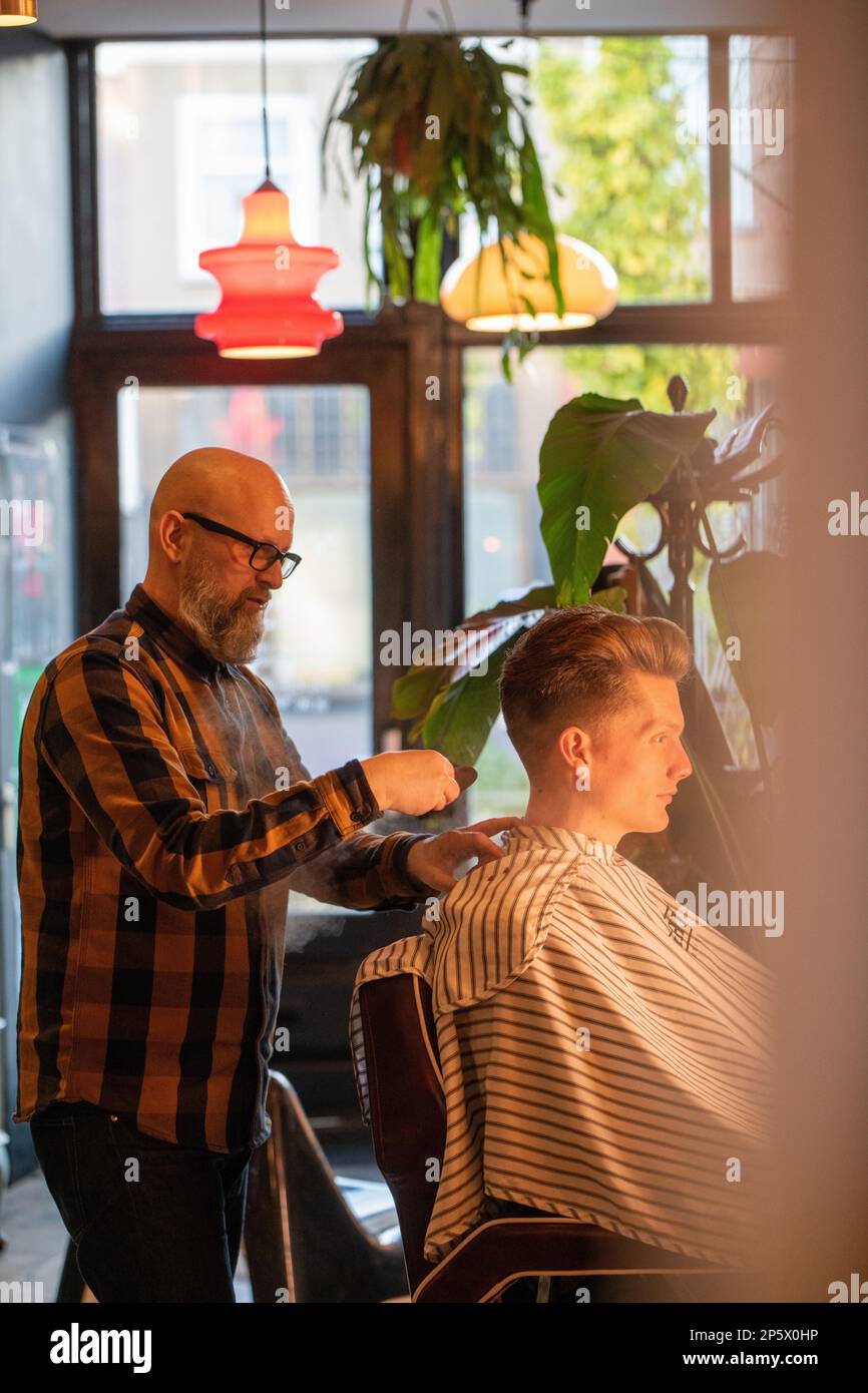 Bearded male barber cutting hair of a client in a Stock Photo Alamy