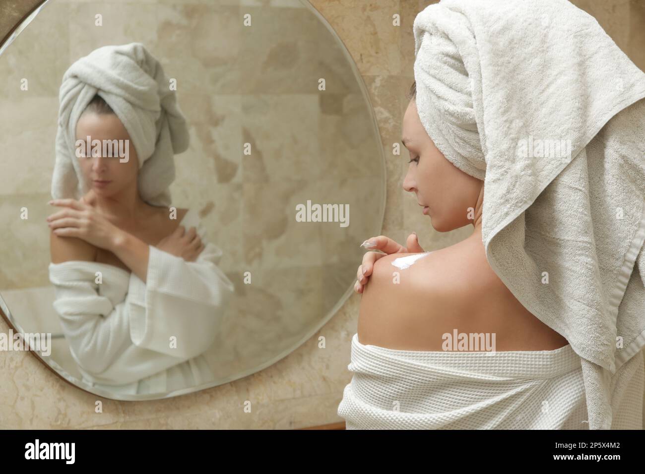 Woman applying body lotion to moisturize her skin after shower, beauty