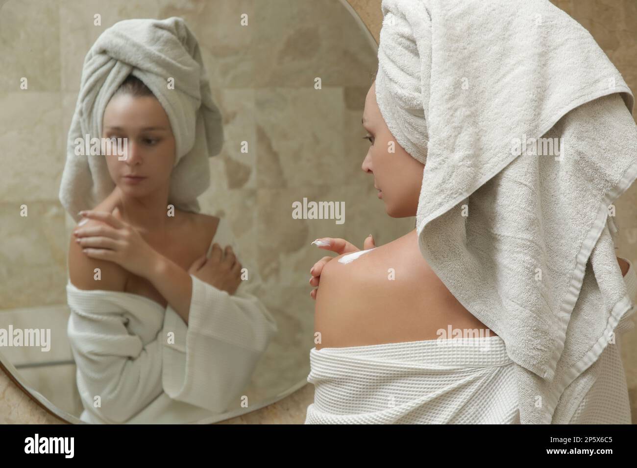 Woman applying body lotion to moisturize her skin after shower, beauty