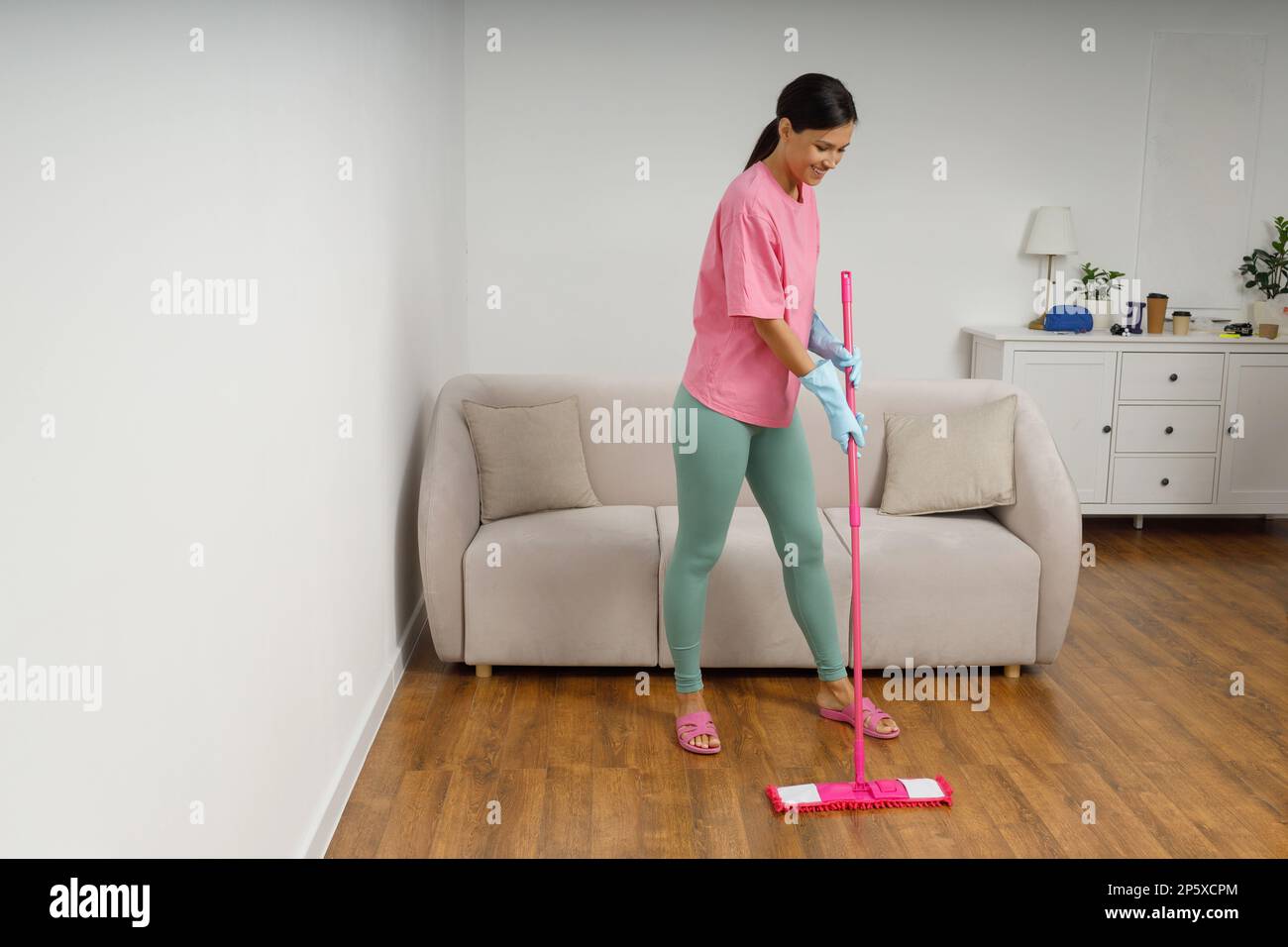 Full-size picture of happy smiling girl doing house cleaning. Washing floors. Cute young woman in casual clothes and rubber gloves wipes the floor wit Stock Photo