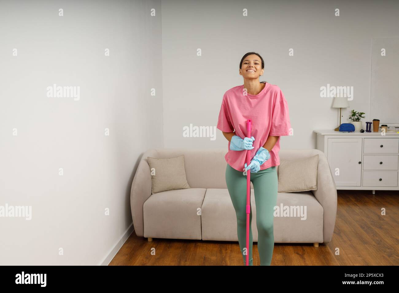 Full-size picture of happy smiling girl doing house cleaning. Washing floors. Cute young woman in casual clothes and rubber gloves wipes the floor wit Stock Photo