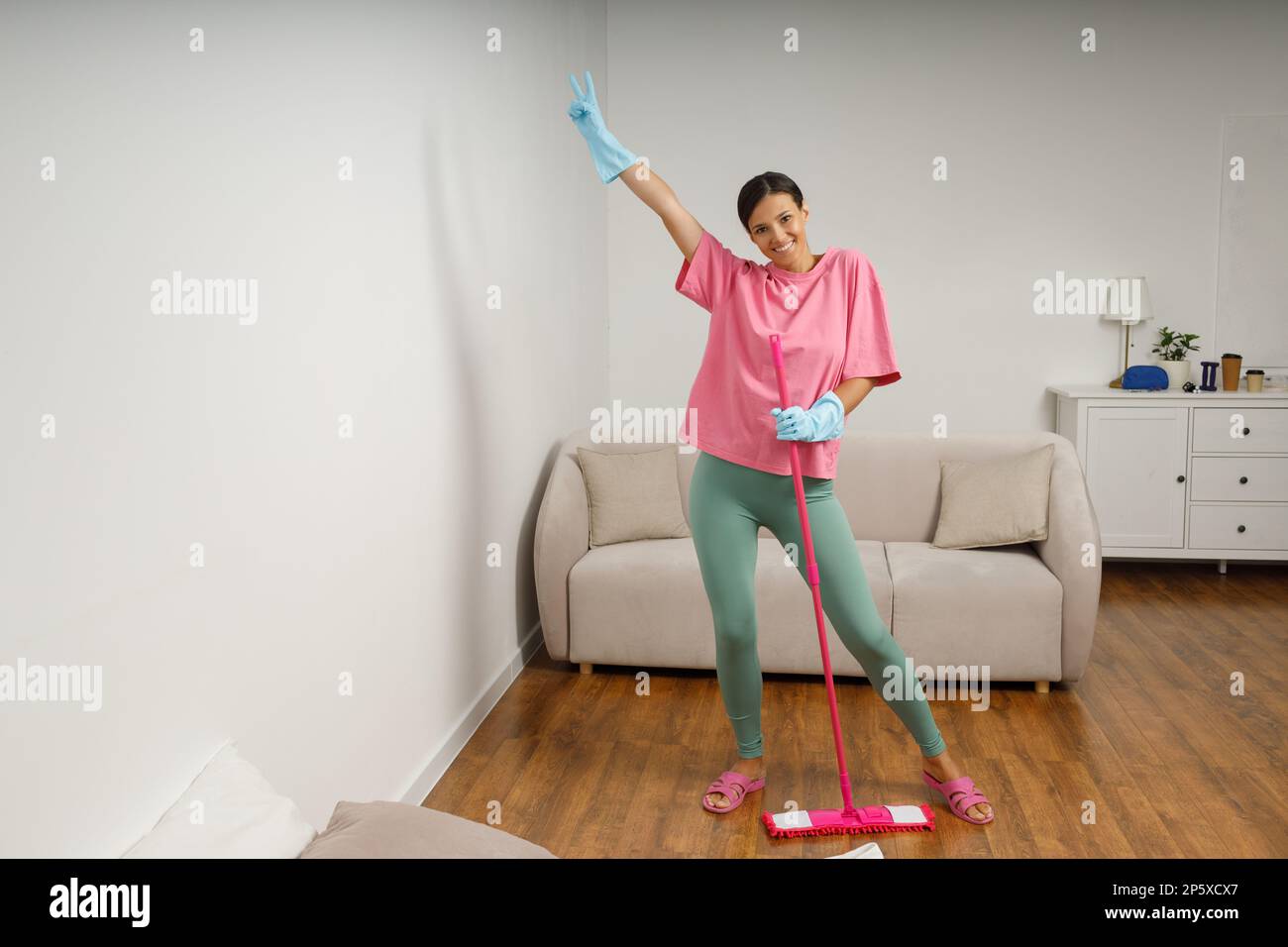 Full-size picture of happy smiling girl doing house cleaning. Washing floors. Cute young woman in casual clothes and rubber gloves wipes the floor wit Stock Photo