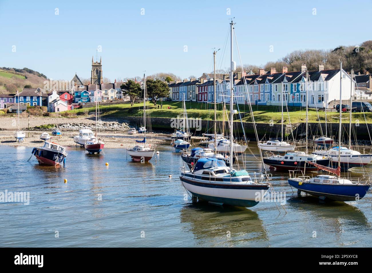 View along Afon Aeron River estuary to church with boats moored in harbour on an incoming tide in attractive seaside town. Aberaeron Ceredigion Wales Stock Photo