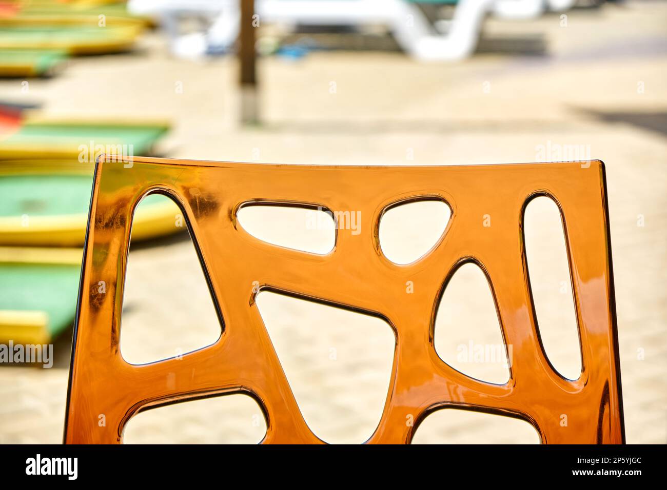 Back of chair made of transparent acrylic glass on blurred background. Place to sit in touristic street cafe near water park on sunny day closeup Stock Photo