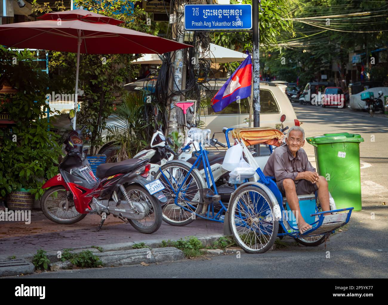 An elderly cyclo driver waits with his pedicab for a passenger on a street corner in Phnom Penh, Cambodia. Stock Photo