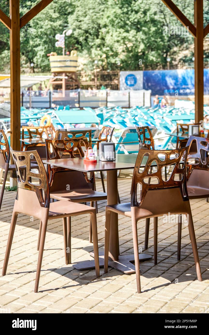 Outdoor street cafe with designer plastic furniture in aqua park on sunny summer day. Table and chairs with transparent backs under cover Stock Photo