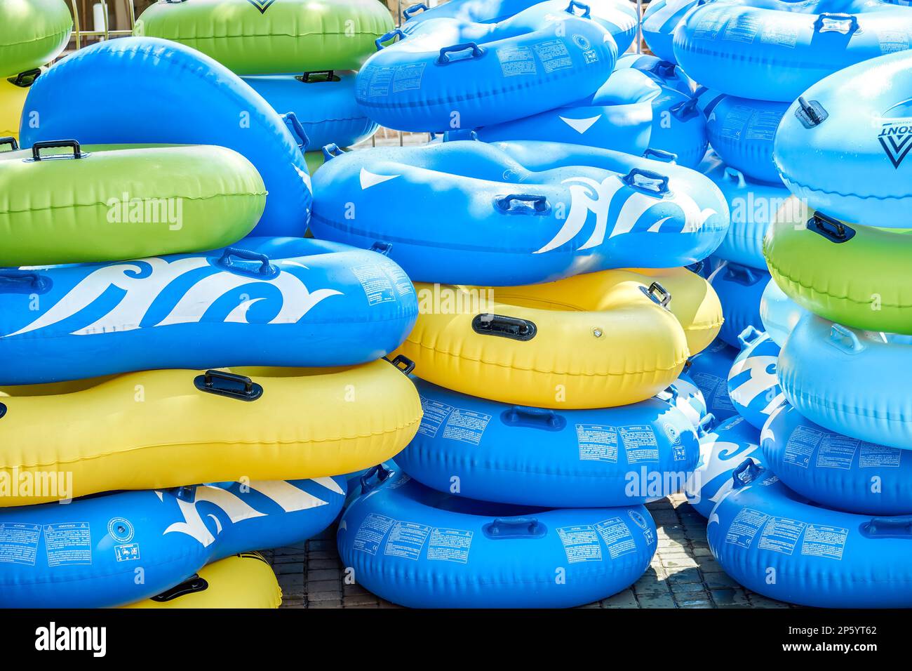 Multi-colored rubber rings for swimming pool put in rows at bright sunlight. Stacks of inflatable swim-rings ready for tourists in water park Stock Photo