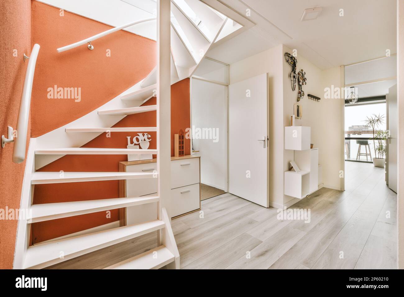 a white and orange room with wood flooring, stairs and an open door
