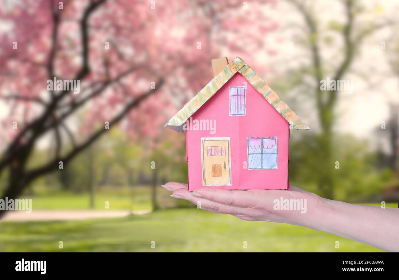 Cute model home on a female hand on blurred beautiful nature and springtime background. Real estate,house purchase, business conccept. Stock Photo