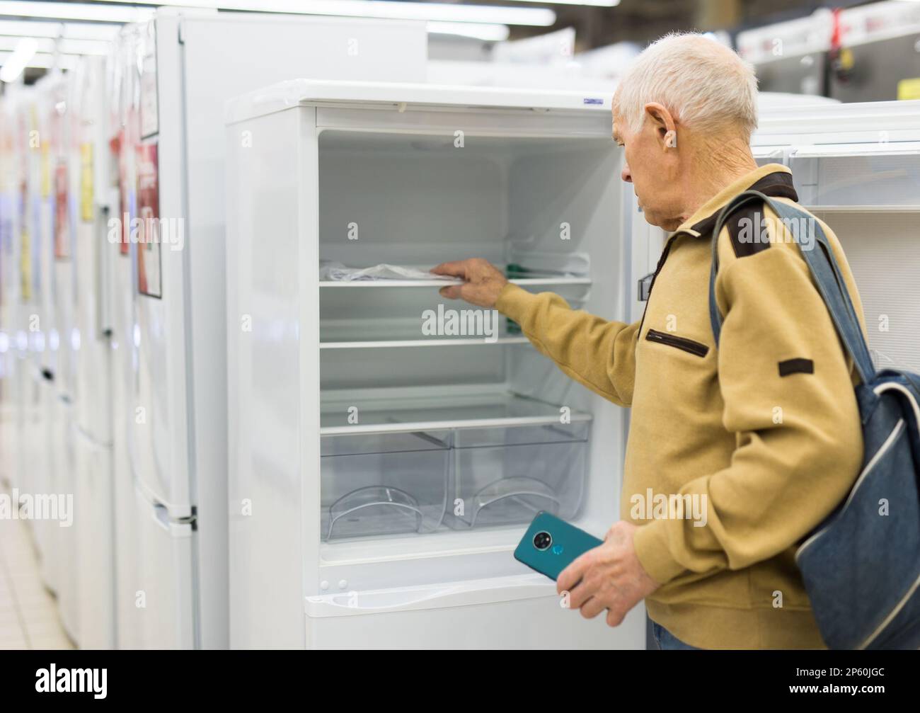 elderly man choosing refrigerator in showroom of electrical appliance
