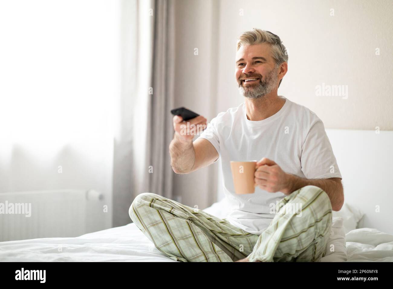 Happy middle aged man watching TV, drinking coffee in bed Stock Photo