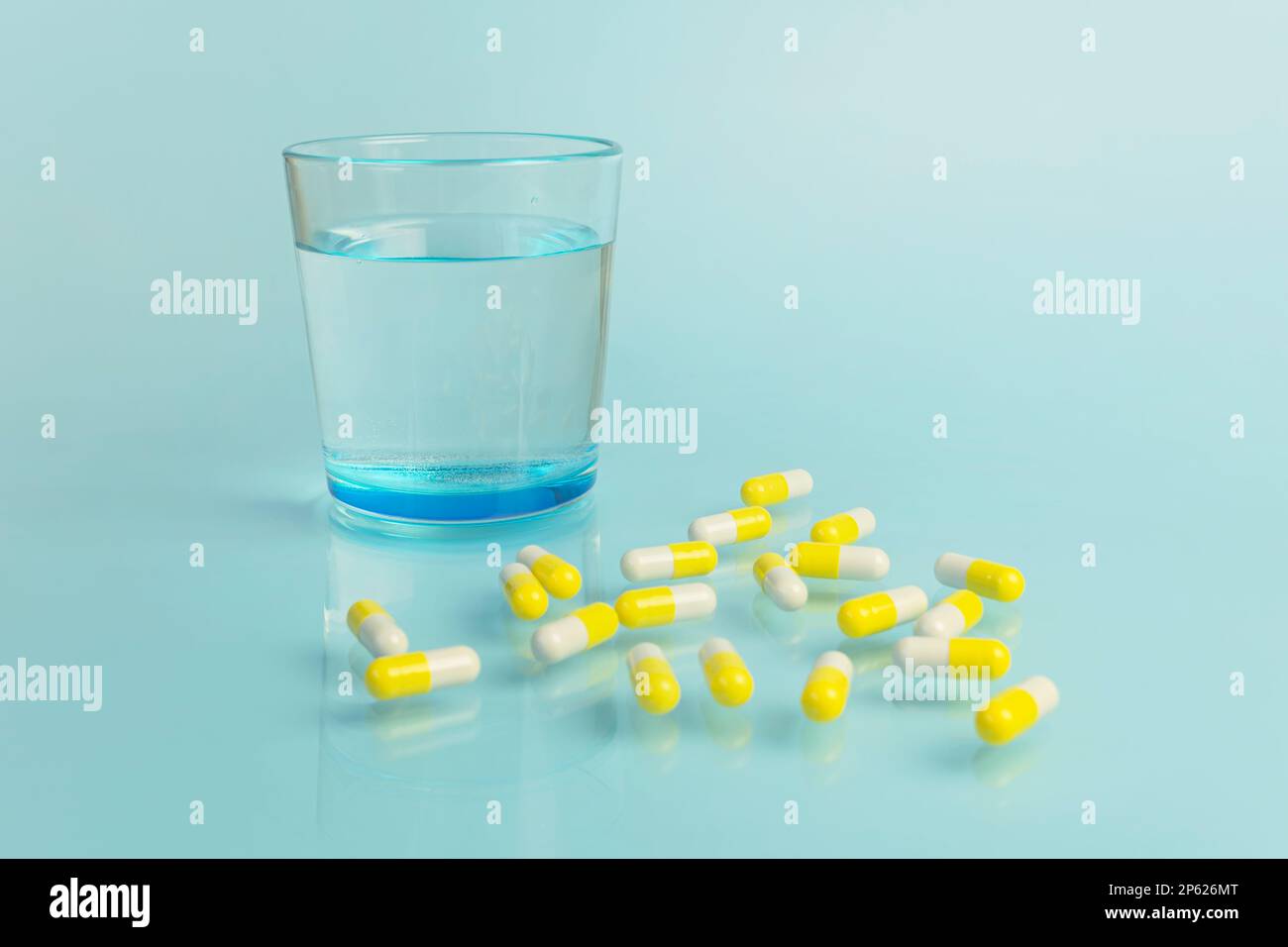 Water glass and white and yellow tablets on blue background. Health and medicine. Copy space. Stock Photo