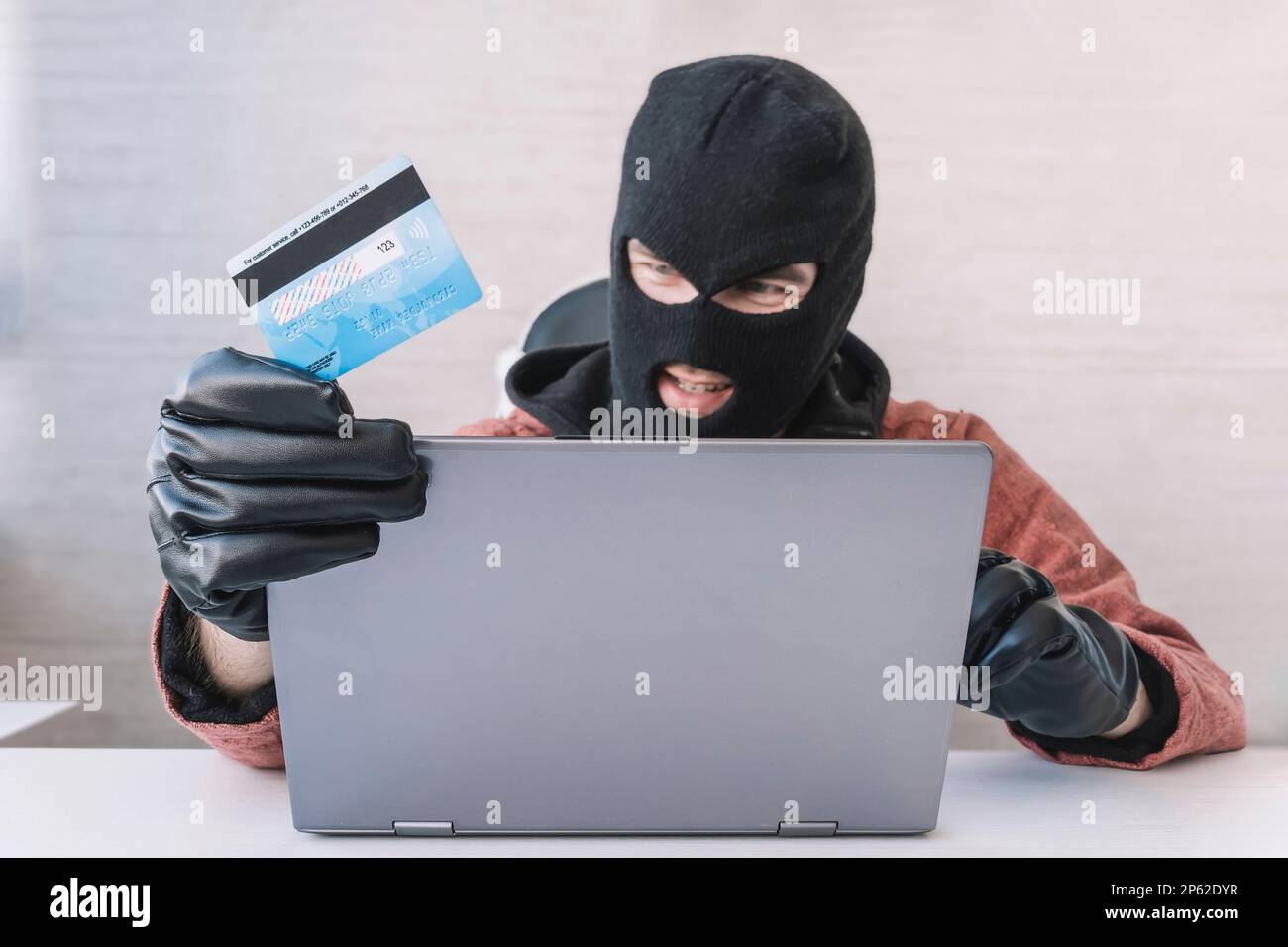 Thieves hold credit cards using a laptop computer for password hacking activities. Cyber crime concepts. a male thief holds a credit card in his hand Stock Photo