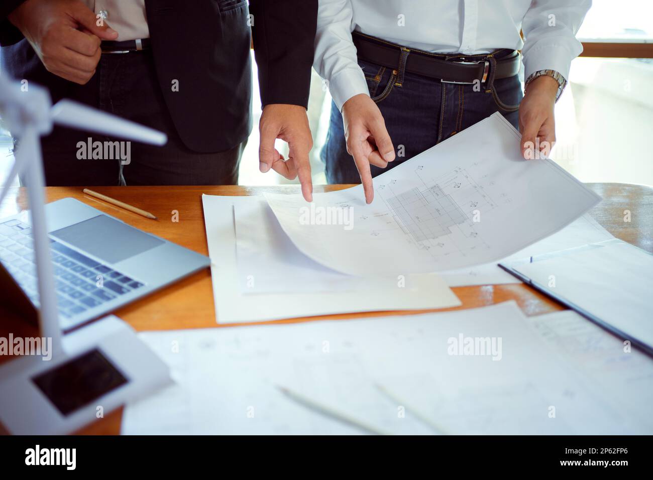 Team of architect and engineer having a discussion while working with wind turbine models and blueprints. Creative businesspeople working on a renewab Stock Photo