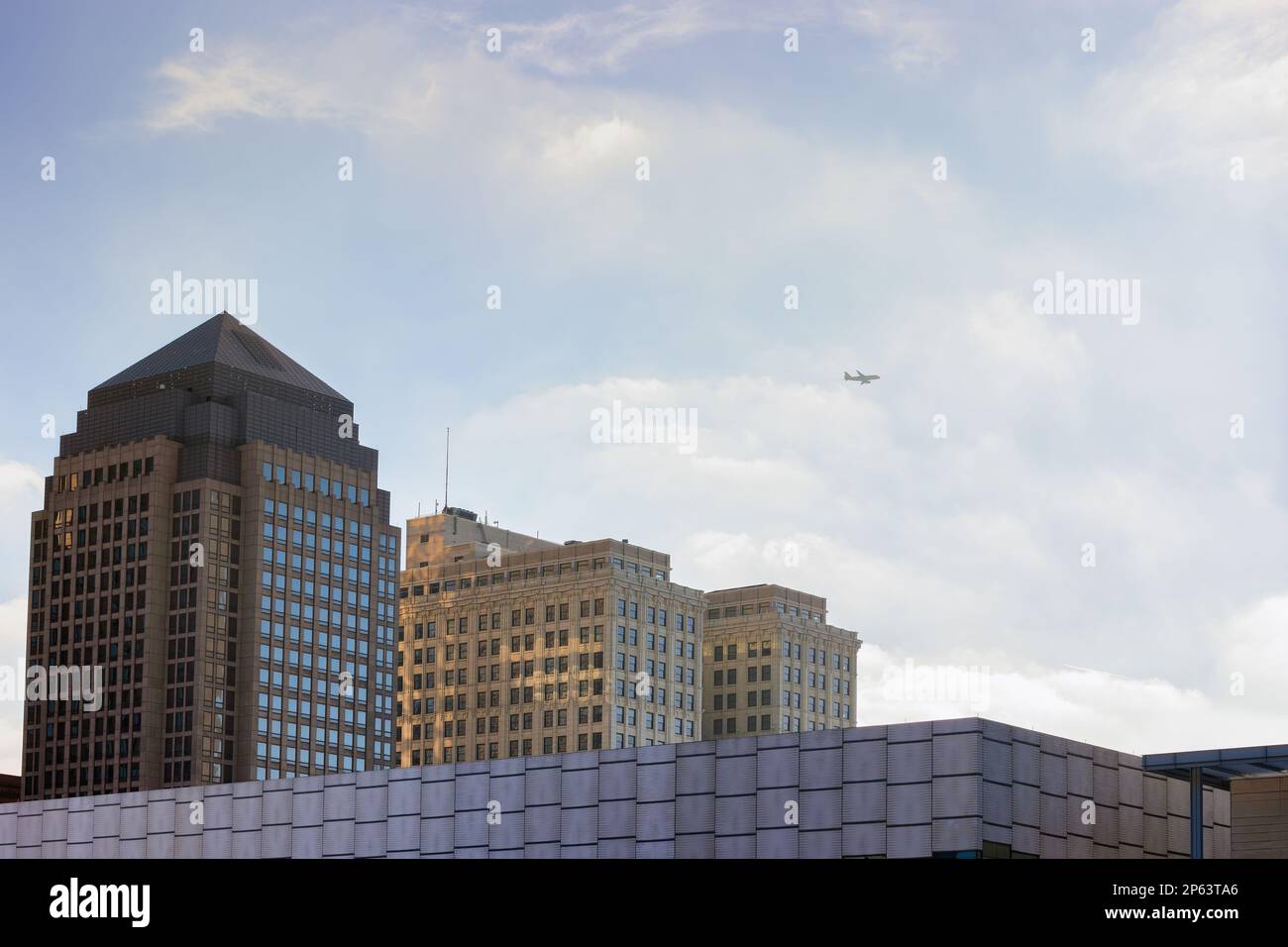 Tops of buildings under cloudy bright skies with a plane flying overhead in downtown Cleveland, Ohio. Stock Photo
