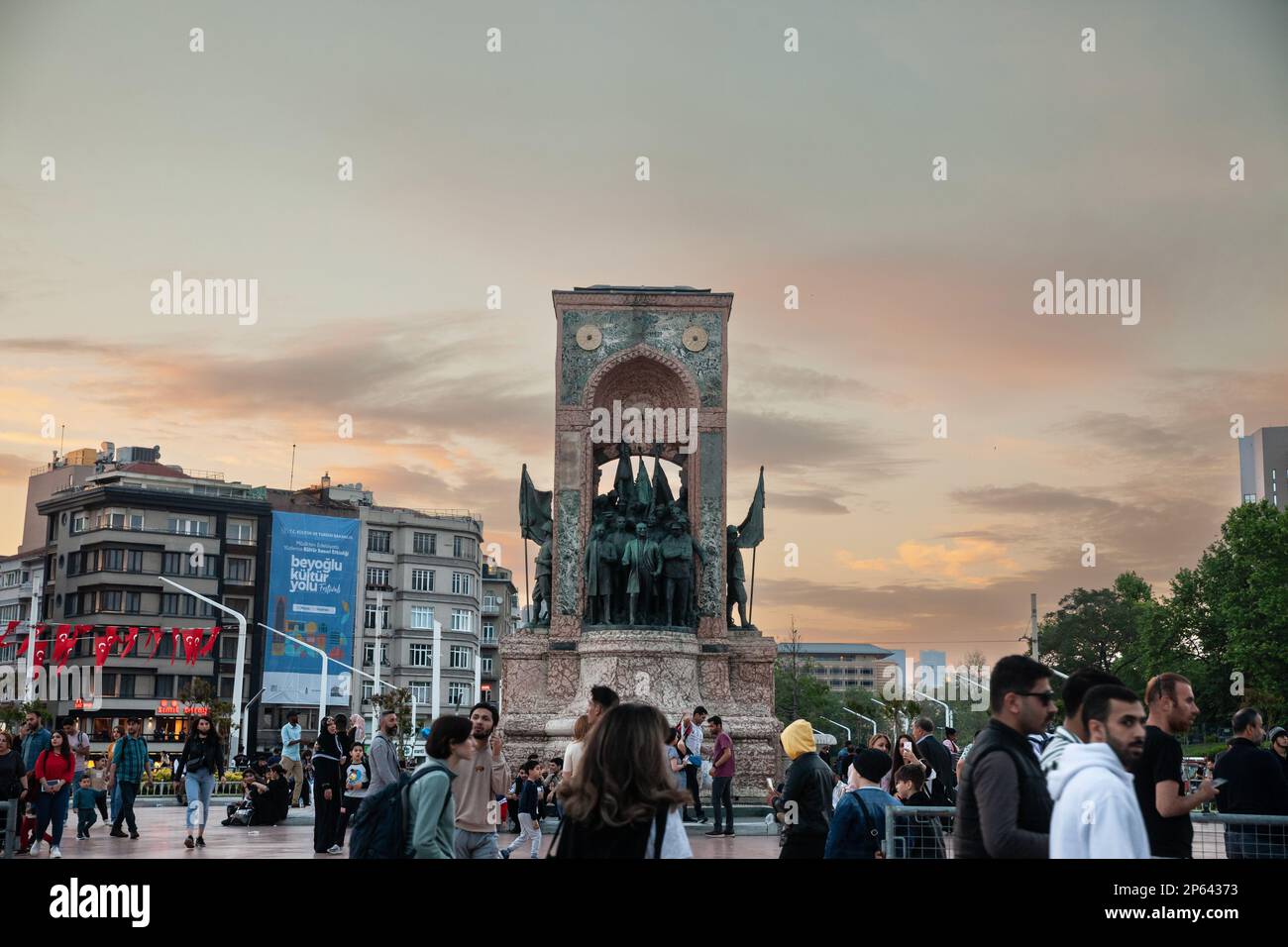 Picture of Taksim Sqaure and Istiklal street, at dusk, focusing on the Republic Monument, with people passing by in front of it. Also known as Monumen Stock Photo
