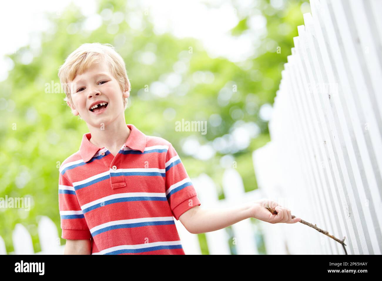 Playing in the backyard. A cute young boy running a stick along a white