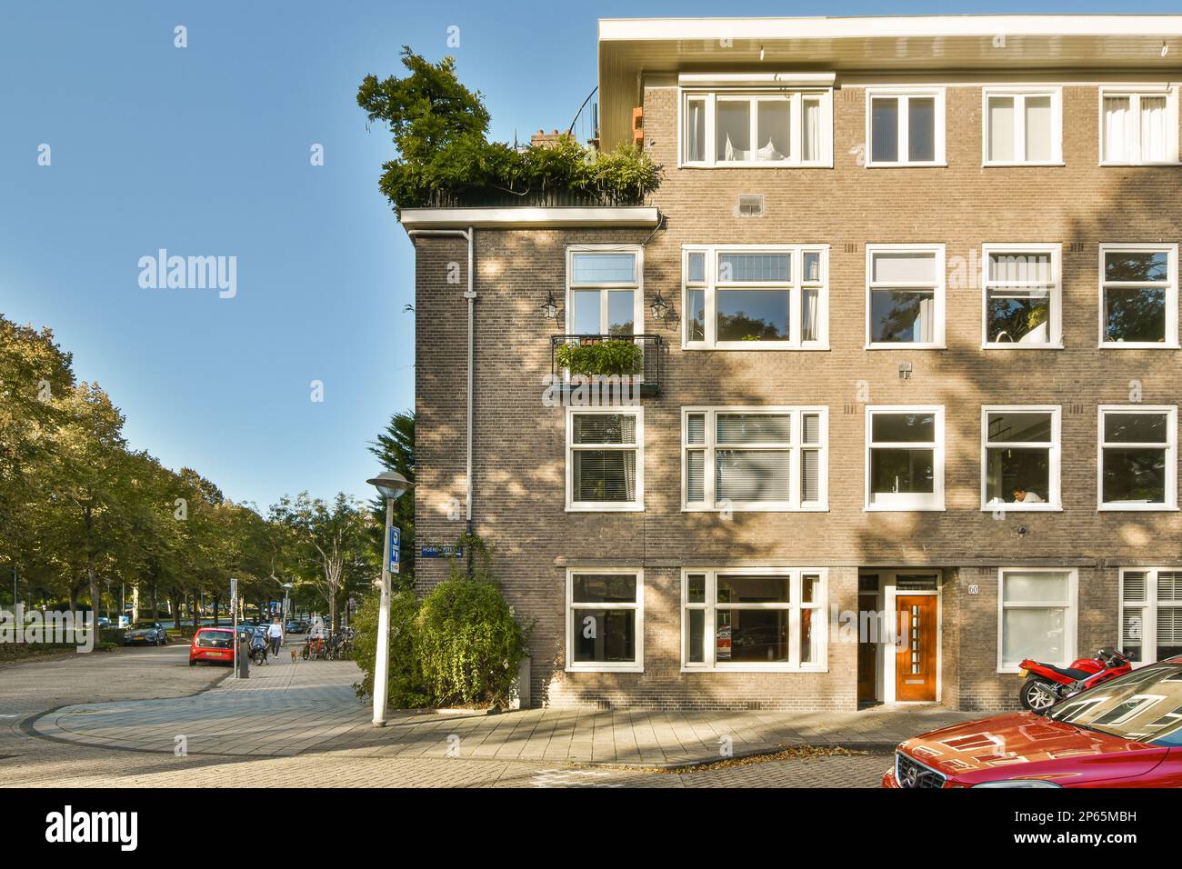 an apartment building with cars parked on the street and people walking ...