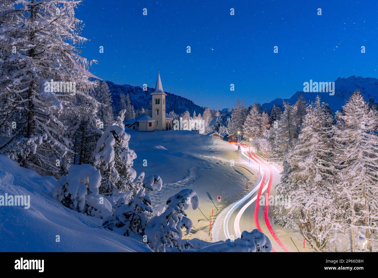 Car trails lights on snowy mountain road leading to Chiesa Bianca under the stars, Maloja, Engadine, Canton of Graubunden, Switzerland, Europe Stock Photo