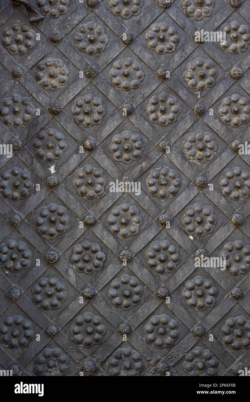 An old metal door, forged gates, rivets on the facade of a cast-iron door, a round handle to open the door, the texture of old iron. High quality phot Stock Photo