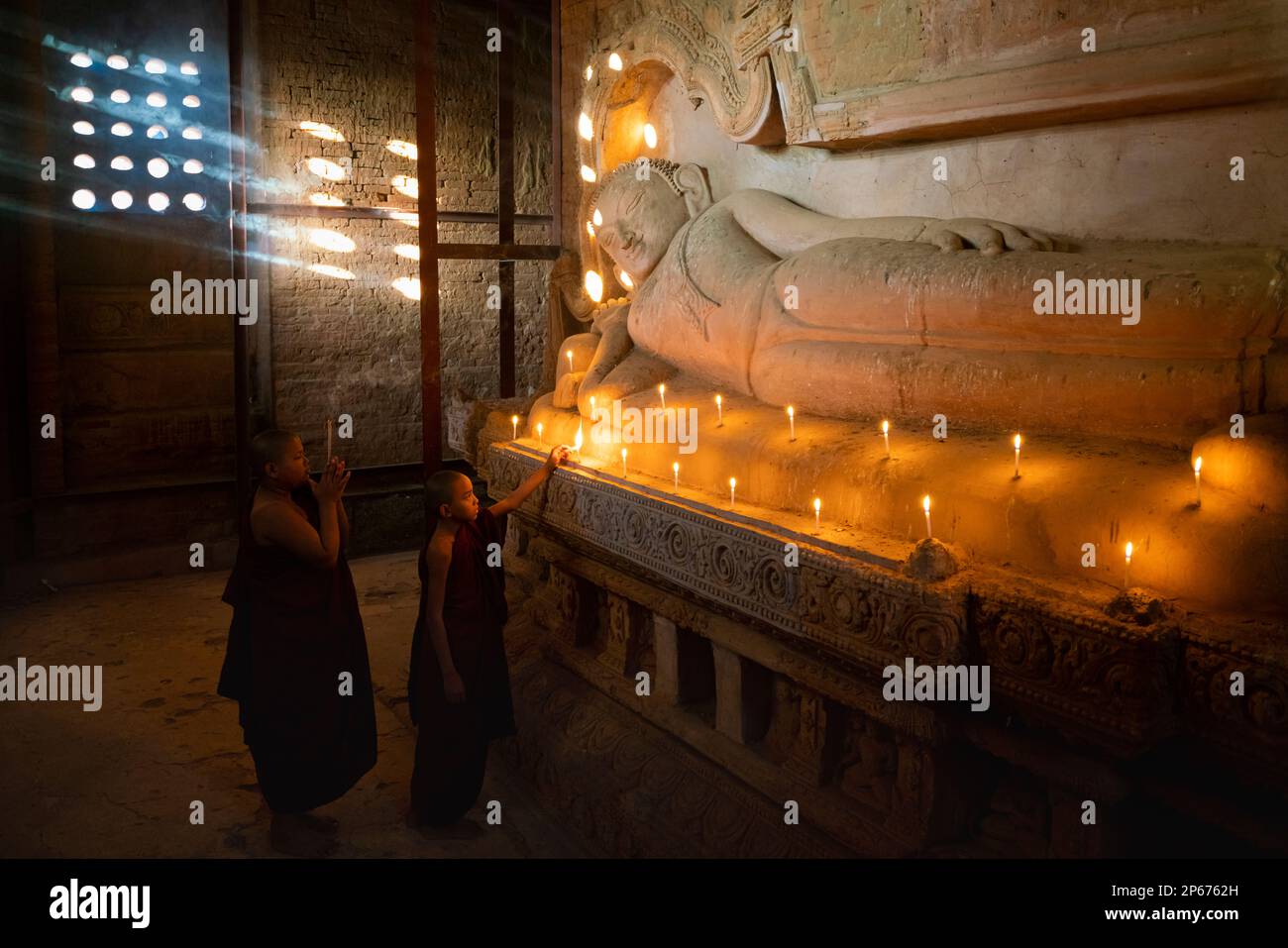 Two novice monks lighting candle by Buddhist statue inside temple, Bagan (Pagan), UNESCO World Heritage Site, Myanmar (Burma), Asia Stock Photo