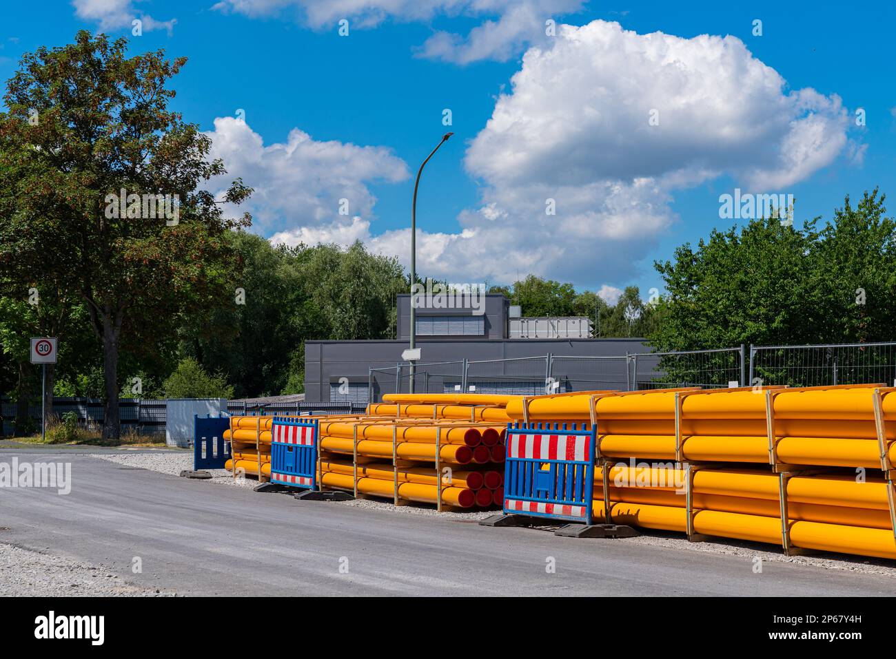 Stack of orang-yellow PVC conduit pipes along the road. Construction site in city. Stock Photo